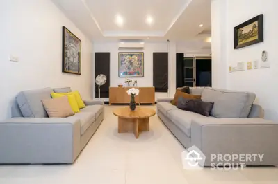 Spacious and modern living room with sleek grey sofas, vibrant throw pillows, and a stylish wooden coffee table, complemented by elegant wall art and pristine white flooring.