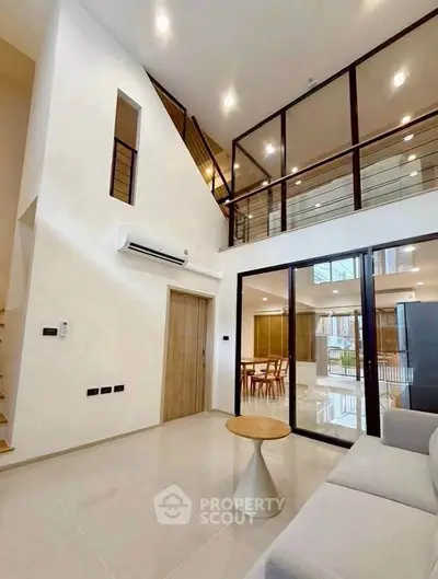 Modern living room with high ceilings and mezzanine, featuring sleek design and natural lighting.