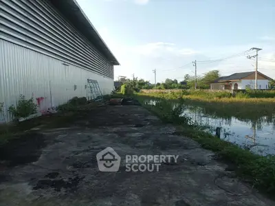 Spacious industrial warehouse exterior with adjacent water feature and lush greenery.