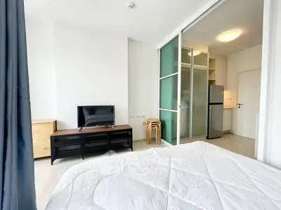 Modern bedroom with TV and glass partition leading to kitchen area.
