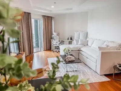 Spacious living room with elegant decor and natural light, featuring a cozy white sofa and stylish workspace.