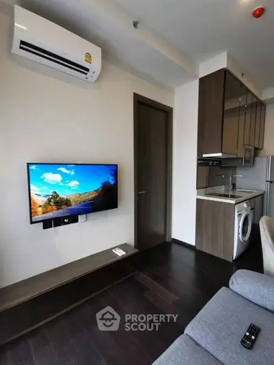 Modern living room with wall-mounted TV and compact kitchen featuring washing machine.