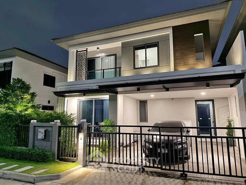 Modern two-story house with sleek design and carport, illuminated at night.