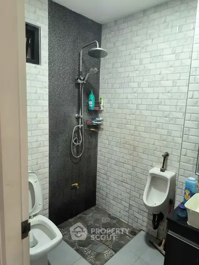 Modern bathroom with shower, toilet, and urinal in sleek tiled design.