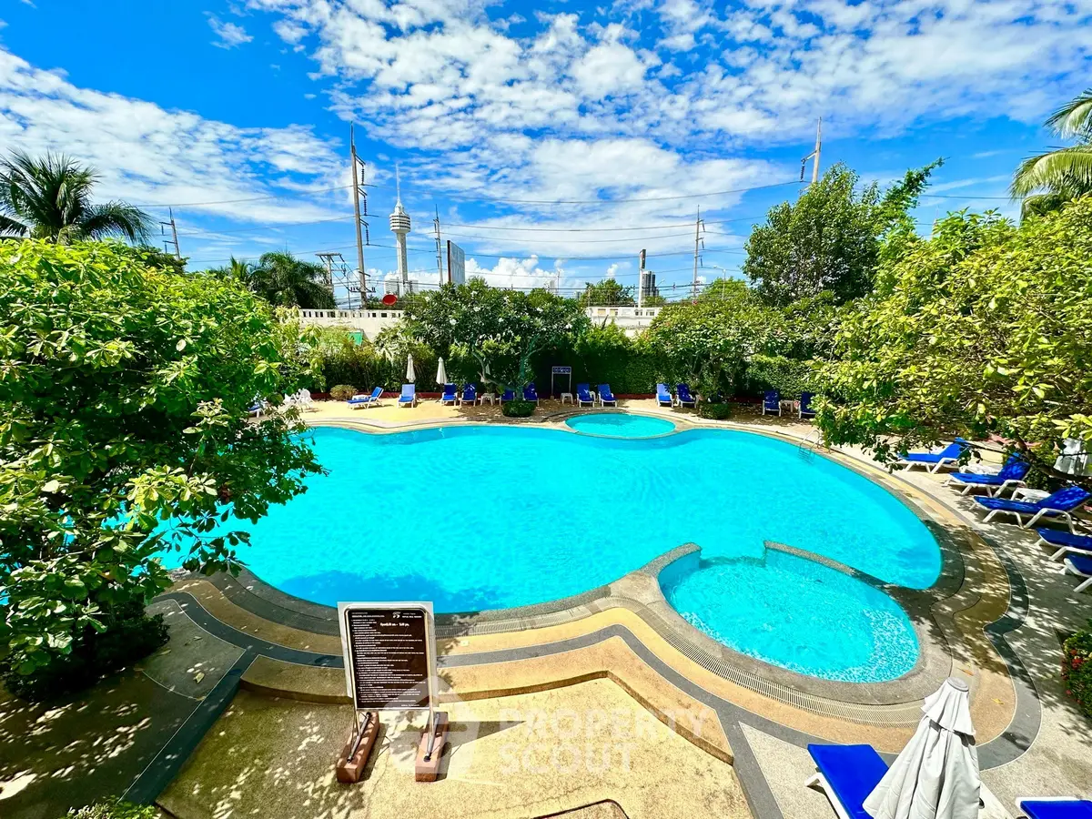 Luxurious outdoor pool with lush greenery and clear blue skies, perfect for relaxation.