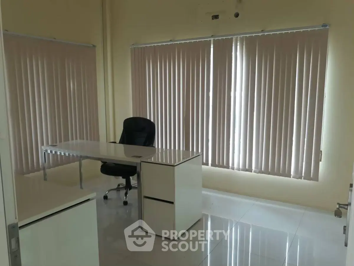 Modern office space with sleek desk and chair, featuring large windows and vertical blinds.