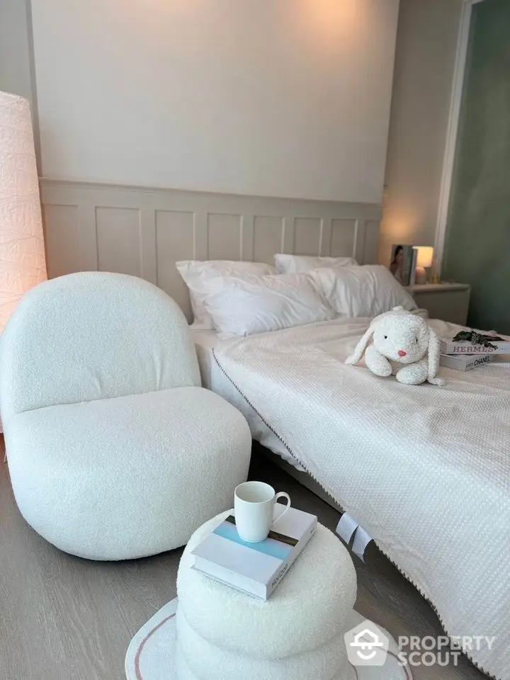 Cozy bedroom with modern white chair and plush bedding, perfect for relaxation.