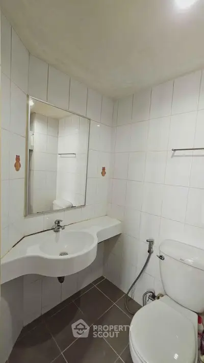 Compact bathroom with white tiles and modern fixtures, featuring a wall-mounted sink and toilet.