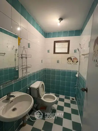 Charming bathroom with teal and white tiles, featuring a sink and toilet, ideal for cozy living spaces.