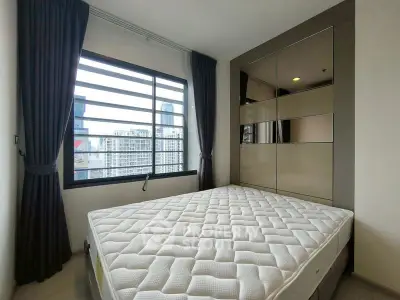 Modern bedroom with large window and city view, featuring a comfortable mattress and sleek wardrobe.