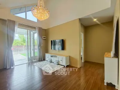 Spacious living room with elegant chandelier and large windows opening to a garden view.