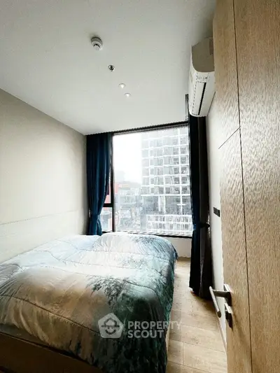 Modern bedroom with large window and city view, featuring cozy bedding and sleek design.