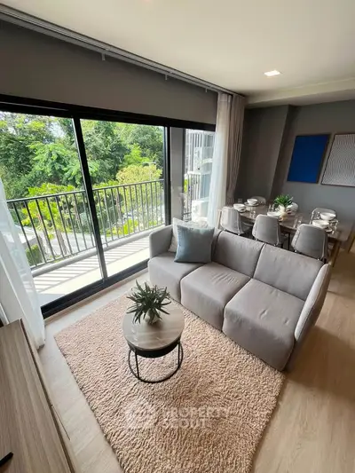 Modern living room with large windows and balcony view, featuring stylish furniture and dining area.