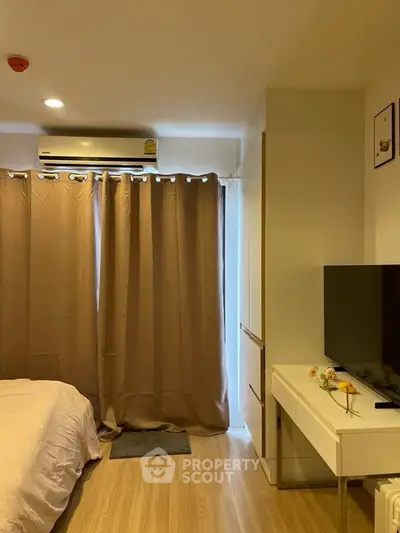Cozy bedroom with modern decor and natural light, featuring a sleek TV setup and elegant curtains.