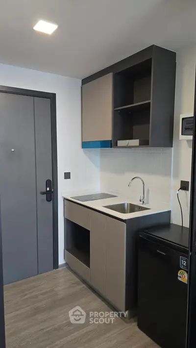 Compact modern kitchen with sleek cabinetry and mini fridge in stylish apartment.