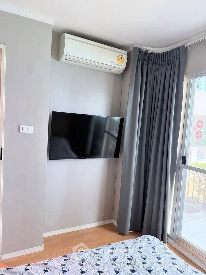 Modern bedroom with wall-mounted TV and air conditioning, featuring large window with curtains.