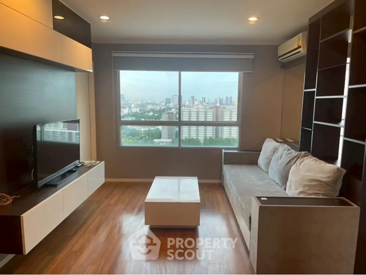 Modern living room with city view, featuring sleek furniture and large window.