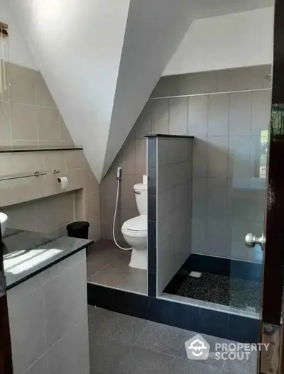 Modern bathroom with sleek tiles and contemporary fixtures under sloped ceiling.