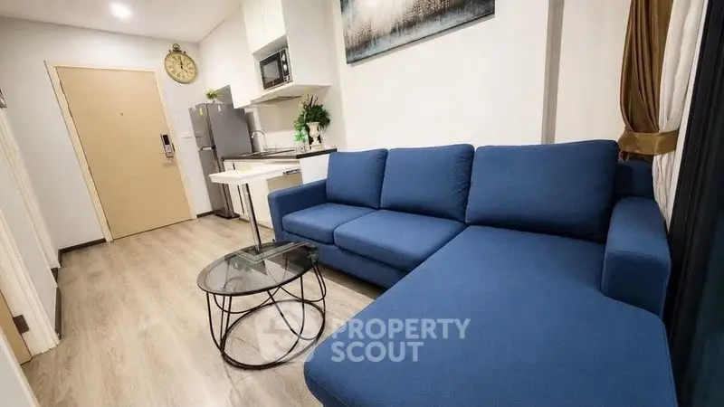 Modern living room with blue sofa and compact kitchen in open layout apartment.