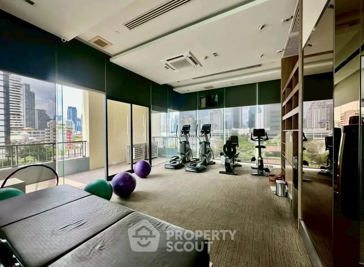 Modern gym with city view, featuring exercise equipment and large windows in a high-rise building.