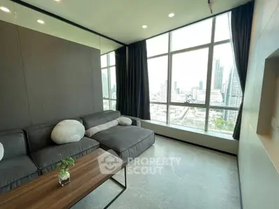 Modern living room with large windows and city view, featuring a sleek gray sofa and minimalist decor.