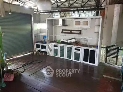 Rustic open kitchen with wooden flooring and metal roof, featuring a simple countertop and storage cabinets.