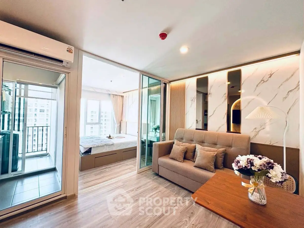Modern living room with stylish decor and view into a cozy bedroom, featuring elegant furniture and natural light.