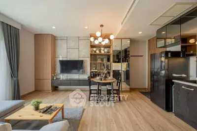 Modern open-layout living room with stylish decor and kitchen area, featuring wooden flooring and contemporary lighting.