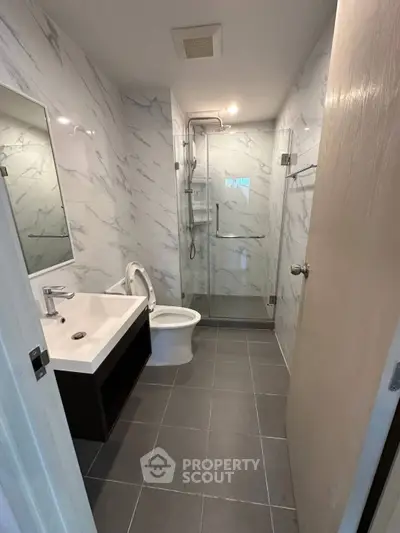Modern bathroom with sleek design, featuring a glass shower enclosure and elegant marble walls.