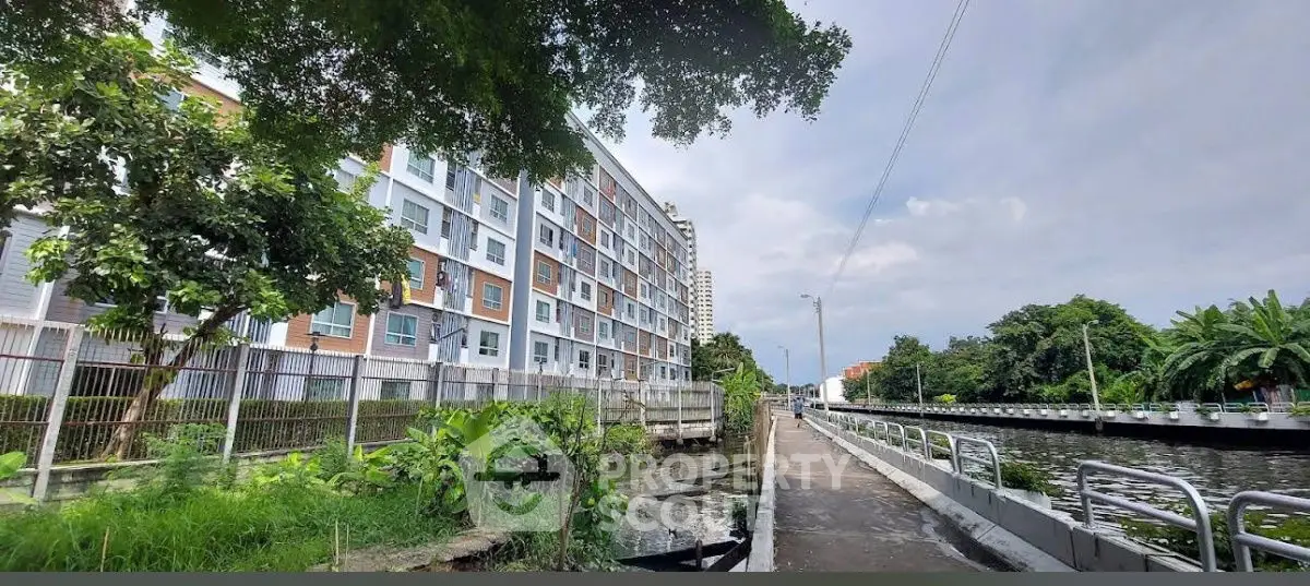 Modern apartment building by a scenic canal with lush greenery and clear skies.