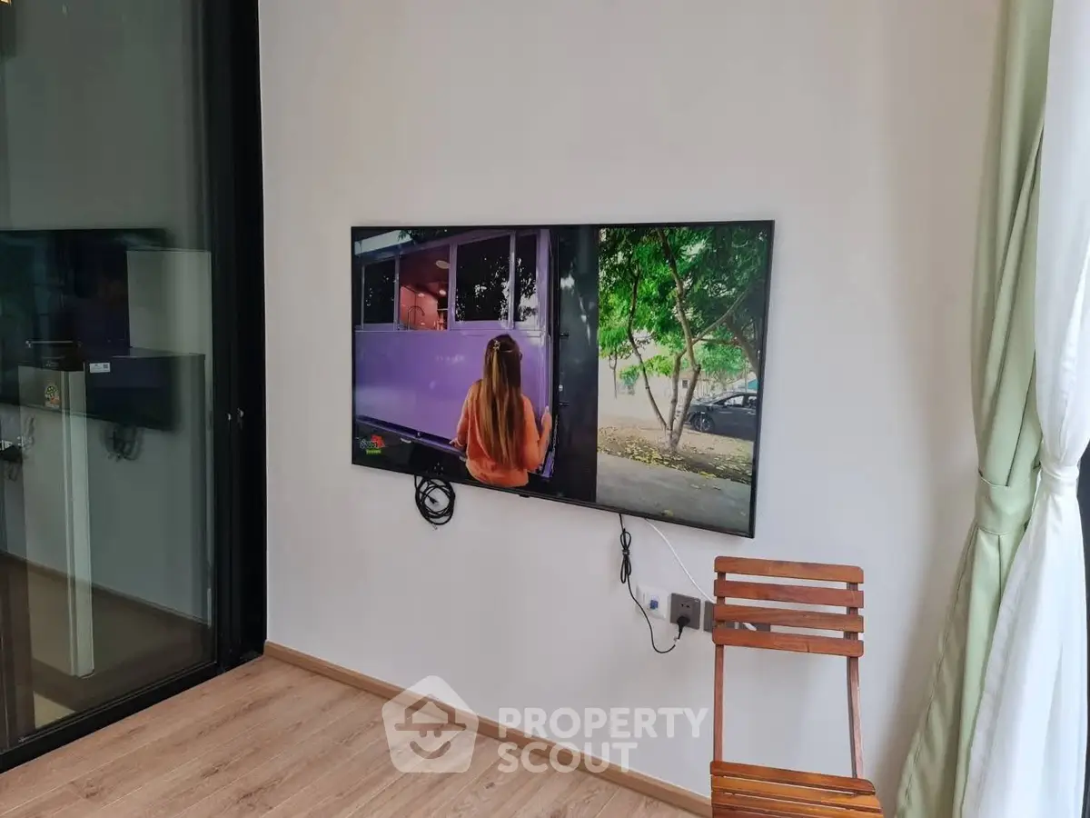 Modern living room with wall-mounted TV and wooden chair, featuring sleek design and natural light.