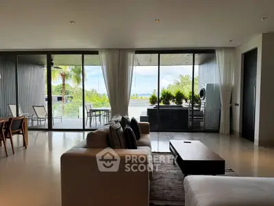 Luxurious living room with expansive glass doors opening to a tropical balcony view, featuring modern furniture and decor.
