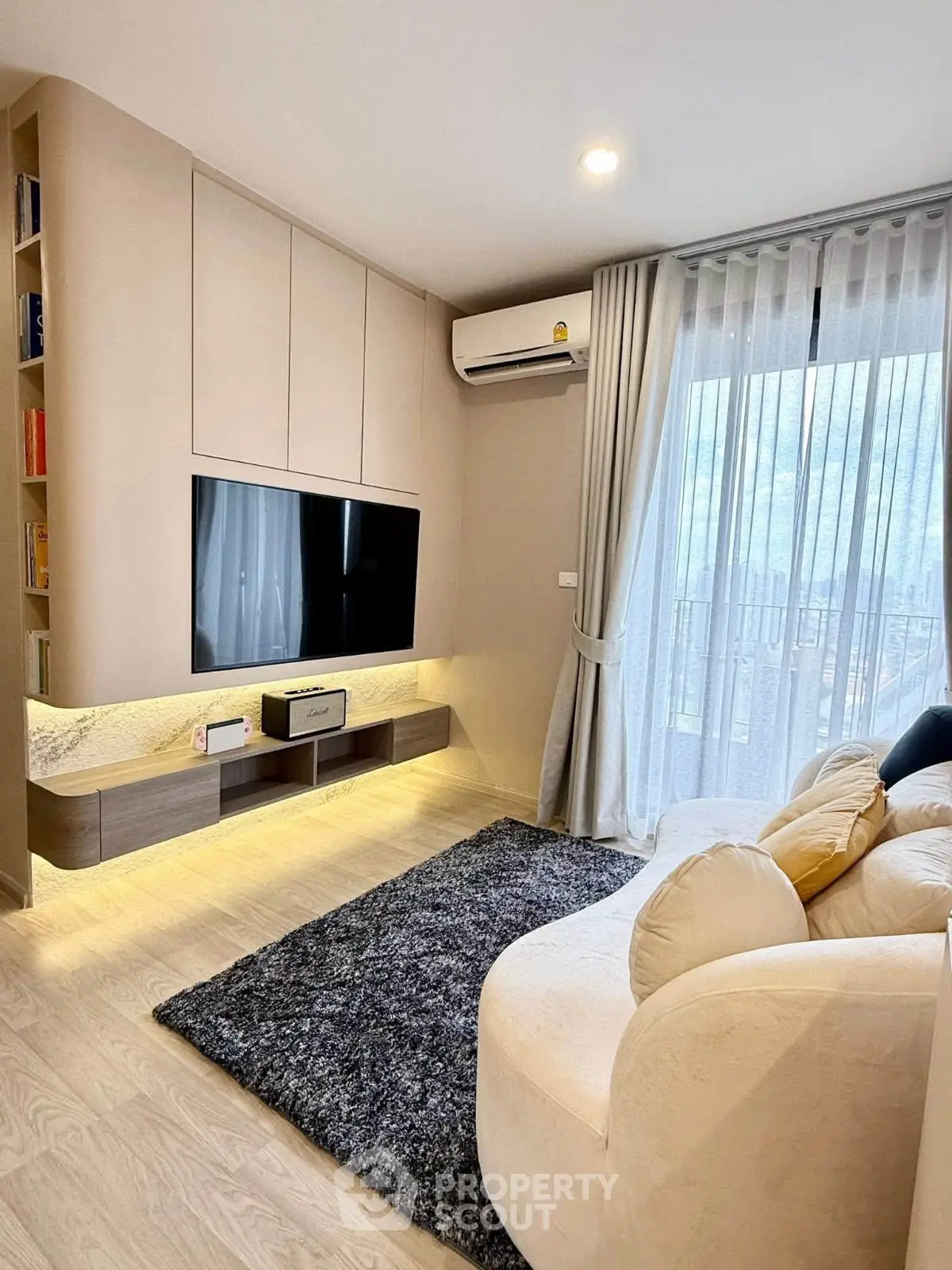Modern living room with cozy sofa, wall-mounted TV, and large window with sheer curtains.