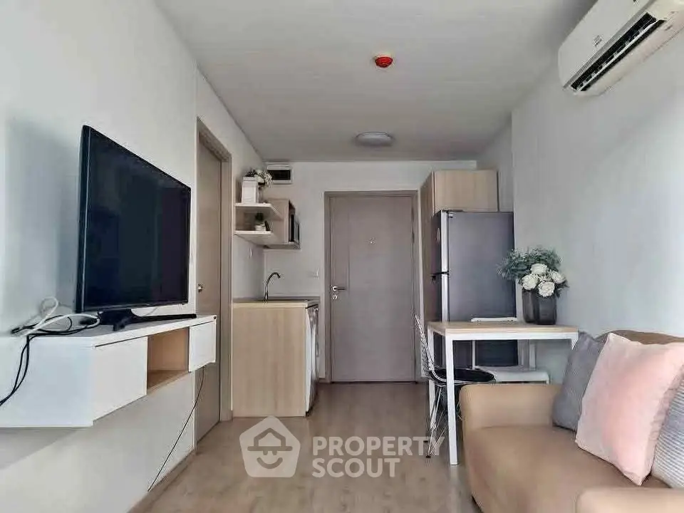 Modern compact living room with kitchen, featuring sleek furniture and air conditioning.