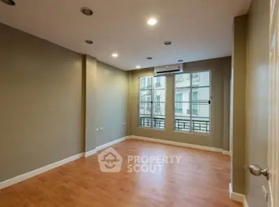 Spacious empty room with wooden flooring and large window in modern apartment.