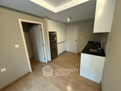 Modern kitchen with sleek design and wooden flooring, featuring a stainless steel fridge and compact layout.