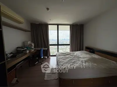 Spacious bedroom with city view, featuring a large window, desk, and comfortable bed.
