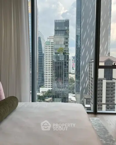 Luxurious bedroom with stunning city view from floor-to-ceiling windows in high-rise building.