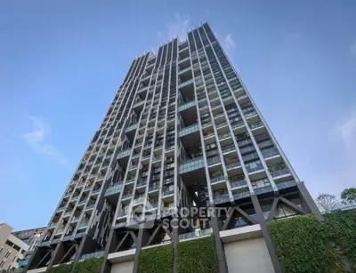 Modern high-rise building with unique architectural design and lush greenery at the base.