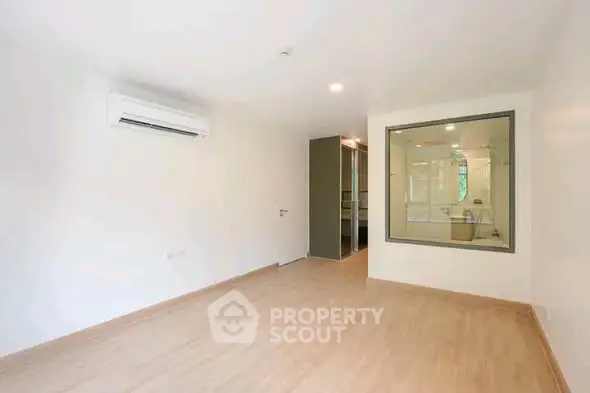 Spacious empty room with wooden flooring and large window, ideal for customization.