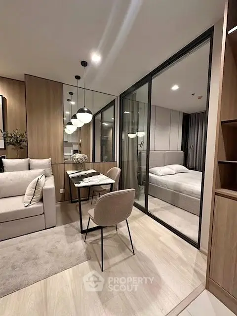 Modern apartment interior with open living and dining area, featuring stylish furniture and glass partition to bedroom.