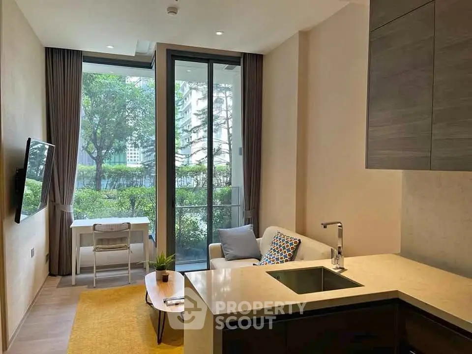 Modern living room with open kitchen and large windows overlooking greenery.