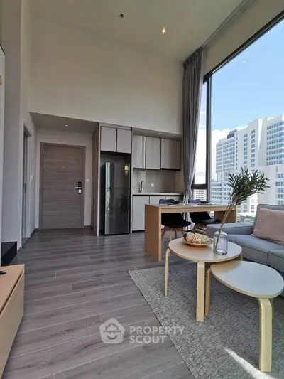 Modern living room with high ceiling and city view, featuring sleek furniture and open kitchen layout.