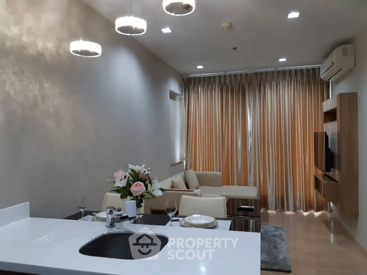Modern living room with open kitchen, elegant lighting, and cozy seating area.