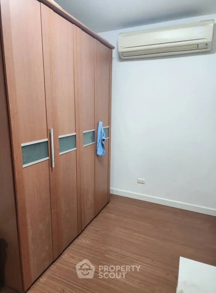 Spacious bedroom with wooden wardrobe and air conditioning unit, perfect for comfortable living.