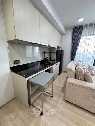 Modern kitchen with sleek cabinetry and cozy living area in open layout apartment.