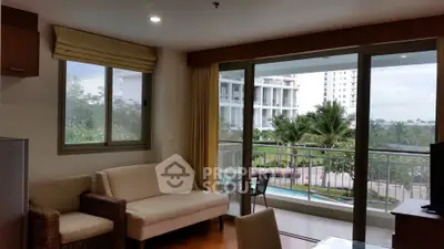 Spacious living room with balcony overlooking lush garden and pool view