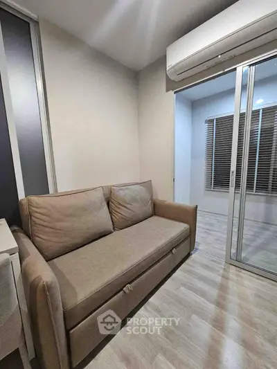 Cozy living room with sofa and air conditioning, featuring sliding glass doors and wooden flooring.
