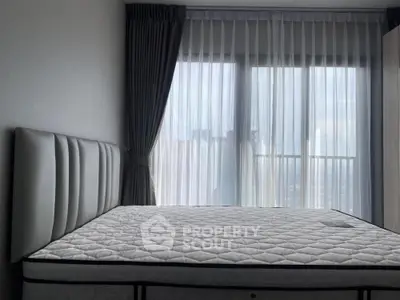 Modern bedroom with large window and city view, featuring a stylish bed and elegant curtains.