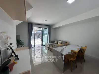 Modern living room with sleek marble dining table and cozy seating area, featuring large windows for natural light.
